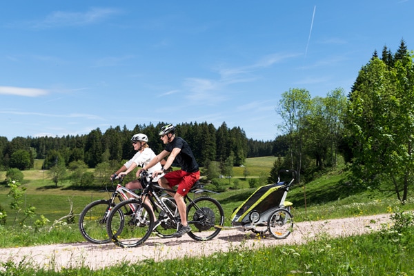 Familie fährt auf E-Mountainbikes mit Anhänger durch Schwarzwaldlandschaft